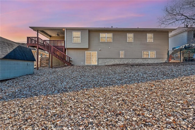 back of property at dusk featuring ceiling fan, an outbuilding, stairs, and fence