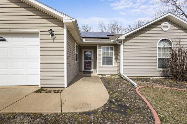 view of exterior entry with a garage, a shingled roof, and solar panels