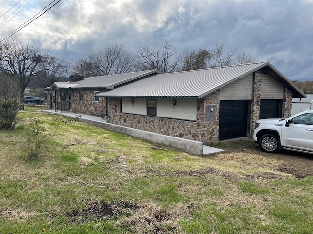 view of side of property featuring stone siding, a chimney, metal roof, an attached garage, and a yard