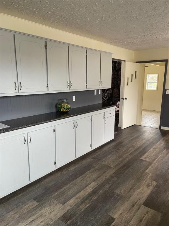 kitchen with a textured ceiling, dark wood-style flooring, and dark countertops