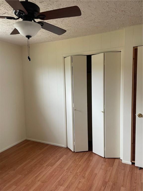 unfurnished bedroom with light wood-style floors, a closet, a ceiling fan, and a textured ceiling