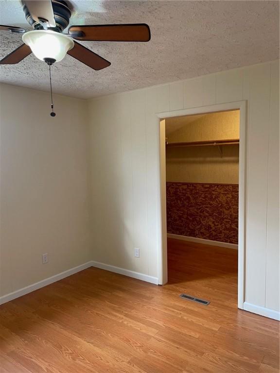 unfurnished bedroom with visible vents, light wood-style flooring, a ceiling fan, a textured ceiling, and baseboards