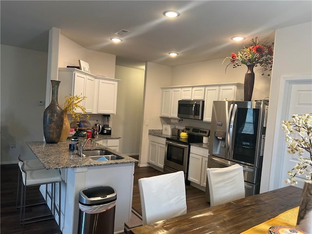 kitchen with stone counters, appliances with stainless steel finishes, white cabinets, a sink, and a peninsula