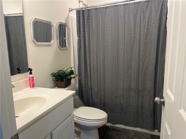 bathroom featuring a shower with shower curtain, a textured wall, vanity, and toilet