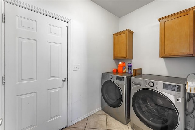 clothes washing area with light tile patterned floors, washer and dryer, cabinet space, and baseboards