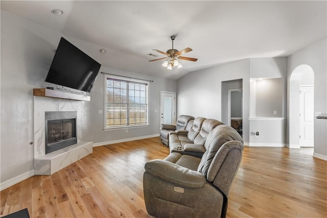 living room with a high end fireplace, baseboards, light wood-type flooring, vaulted ceiling, and a ceiling fan