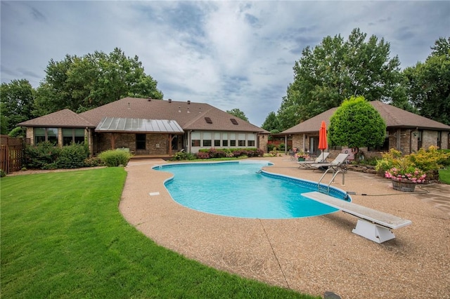 outdoor pool with a patio area, a lawn, fence, and a diving board