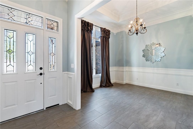 foyer with ornamental molding, a tray ceiling, baseboards, and an inviting chandelier