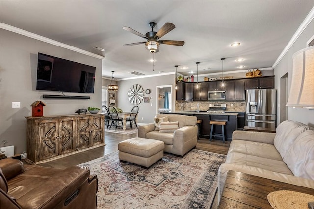 living room featuring a ceiling fan, visible vents, ornamental molding, and wood finished floors