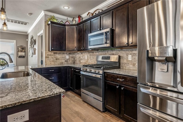 kitchen with light stone counters, stainless steel appliances, a sink, visible vents, and crown molding