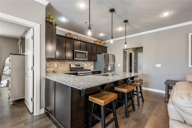 kitchen featuring stainless steel appliances, a breakfast bar, a sink, dark brown cabinets, and backsplash