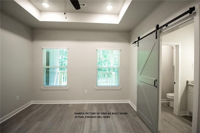 interior space with a barn door, wood finished floors, visible vents, baseboards, and a raised ceiling