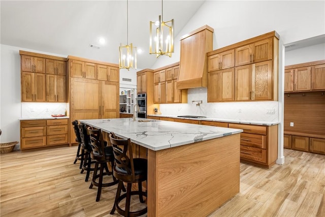 kitchen with light stone countertops, appliances with stainless steel finishes, light wood-type flooring, decorative backsplash, and pendant lighting