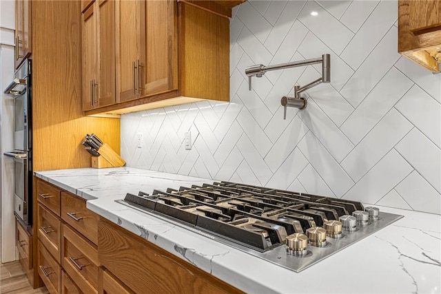 kitchen with stainless steel appliances, decorative backsplash, light stone countertops, and brown cabinets