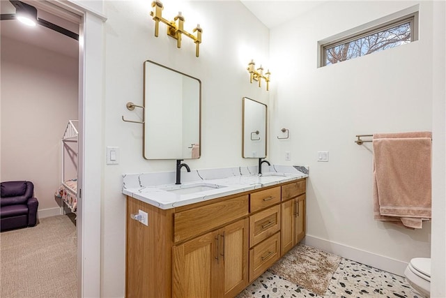 full bathroom featuring double vanity, baseboards, toilet, and a sink