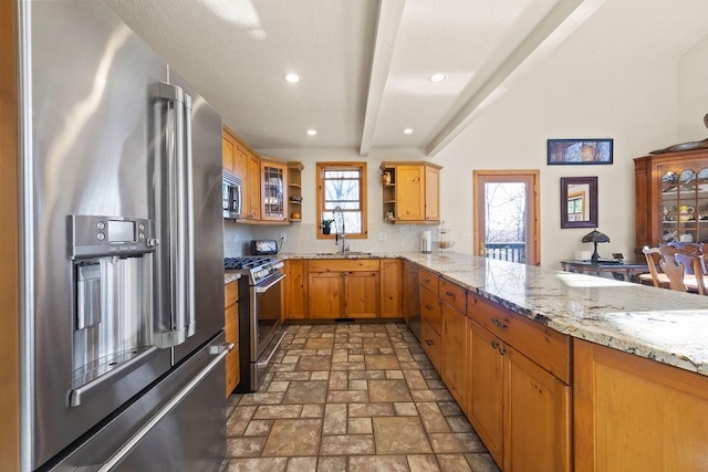 kitchen with a sink, appliances with stainless steel finishes, beam ceiling, open shelves, and stone finish floor