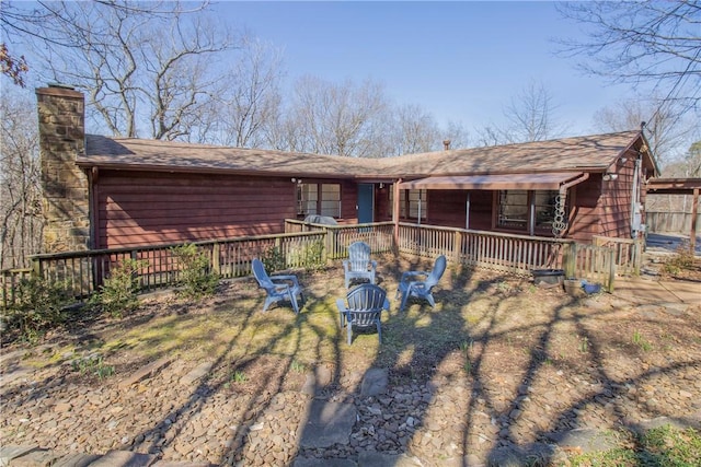 rear view of property featuring a chimney, a wooden deck, and an outdoor fire pit