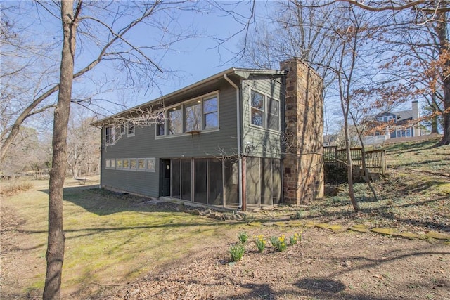 view of property exterior featuring a lawn, a chimney, and a sunroom