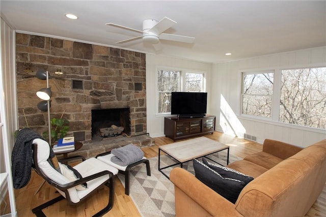 living room featuring recessed lighting, visible vents, a stone fireplace, and wood finished floors