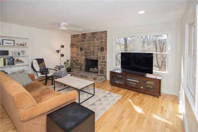 living area with a ceiling fan, a decorative wall, wood finished floors, and a fireplace