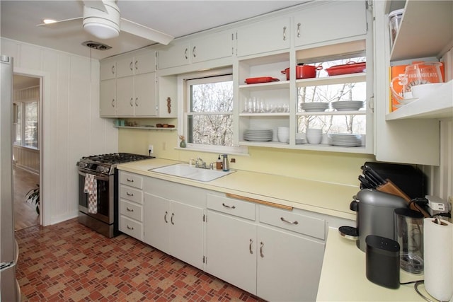 kitchen featuring a ceiling fan, a sink, gas stove, light countertops, and brick floor