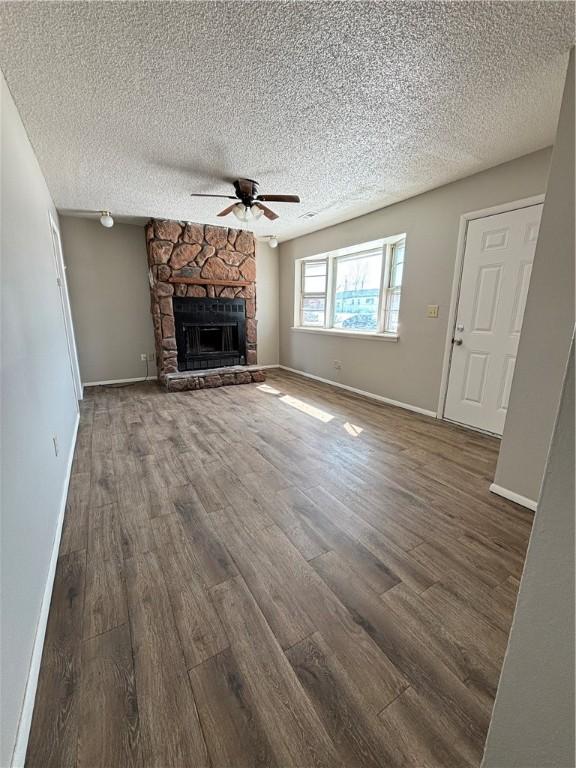 unfurnished living room with baseboards, ceiling fan, wood finished floors, a textured ceiling, and a stone fireplace