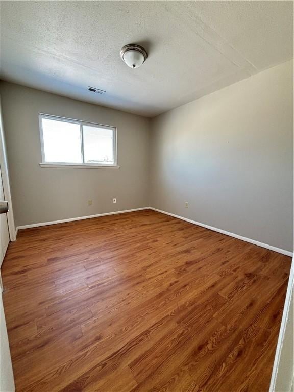 empty room with visible vents, a textured ceiling, baseboards, and wood finished floors