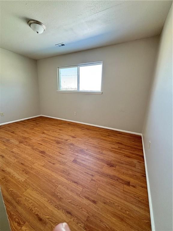 unfurnished room with visible vents, a textured ceiling, baseboards, and wood finished floors