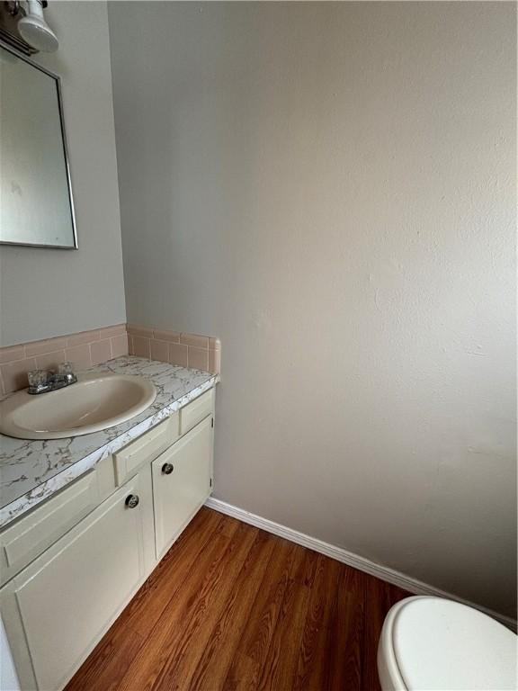 half bathroom with toilet, vanity, baseboards, and wood finished floors