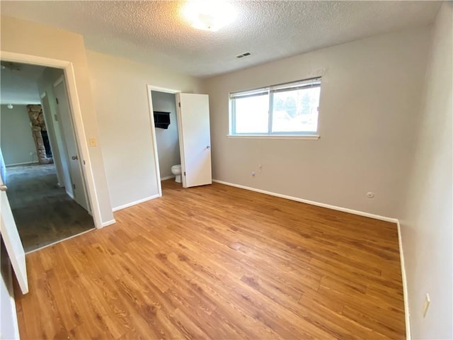 unfurnished bedroom with light wood-style flooring, a fireplace, visible vents, and a textured ceiling