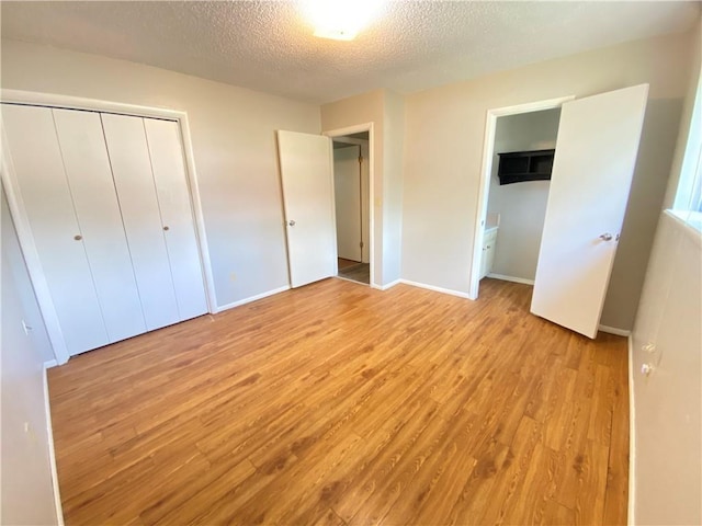 unfurnished bedroom featuring a closet, baseboards, a textured ceiling, and light wood finished floors