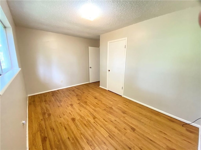 empty room with light wood-type flooring, baseboards, and a textured ceiling