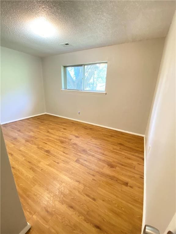 empty room with a textured ceiling, wood finished floors, and baseboards