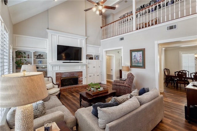 living room with a ceiling fan, a fireplace, visible vents, and dark wood-type flooring