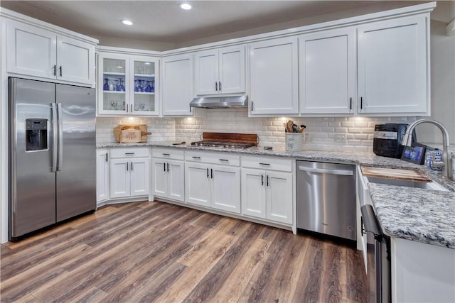 kitchen featuring tasteful backsplash, appliances with stainless steel finishes, white cabinetry, wood finished floors, and under cabinet range hood