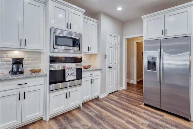 kitchen featuring white cabinets, decorative backsplash, light stone countertops, stainless steel appliances, and light wood-style floors