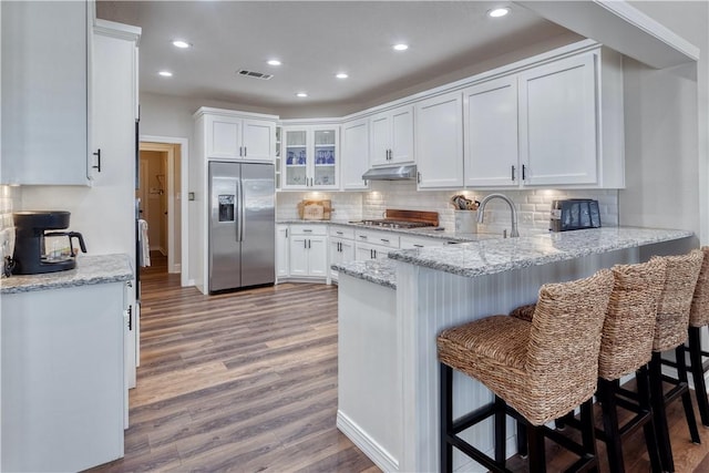 kitchen featuring under cabinet range hood, a peninsula, wood finished floors, appliances with stainless steel finishes, and tasteful backsplash