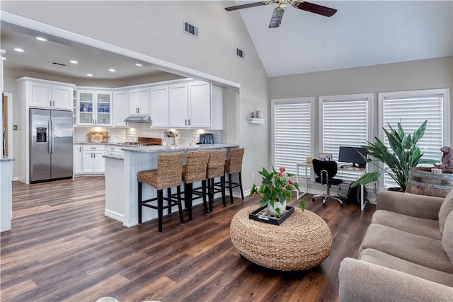 interior space with built in fridge, a peninsula, visible vents, open floor plan, and glass insert cabinets