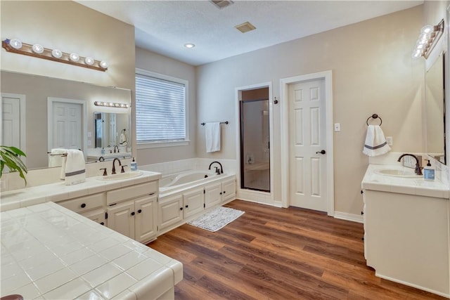 bathroom with a garden tub, a sink, a shower stall, and wood finished floors