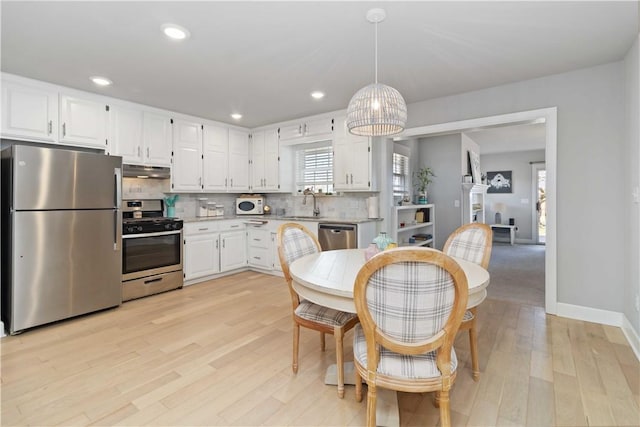 kitchen with light wood-style flooring, under cabinet range hood, backsplash, white cabinetry, and appliances with stainless steel finishes