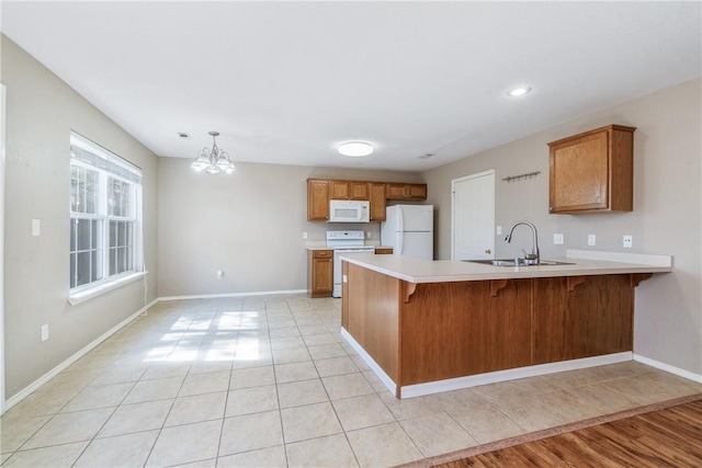 kitchen with white appliances, brown cabinets, a peninsula, light countertops, and a sink