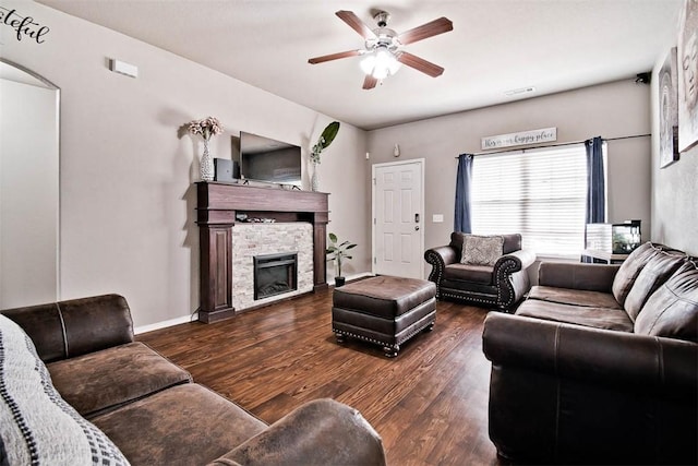 living area featuring visible vents, a ceiling fan, a stone fireplace, wood finished floors, and baseboards