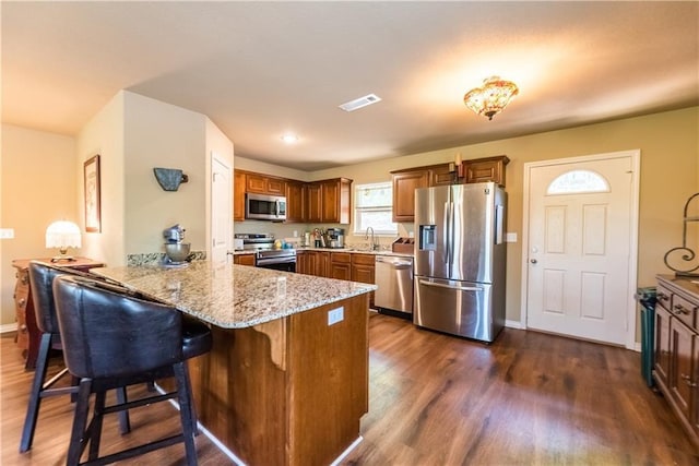 kitchen featuring stainless steel appliances, a peninsula, dark wood-style flooring, visible vents, and light stone countertops