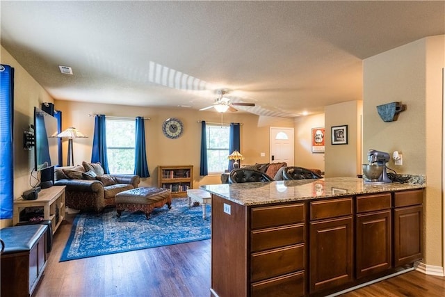 kitchen featuring light stone counters, a peninsula, visible vents, open floor plan, and dark wood finished floors