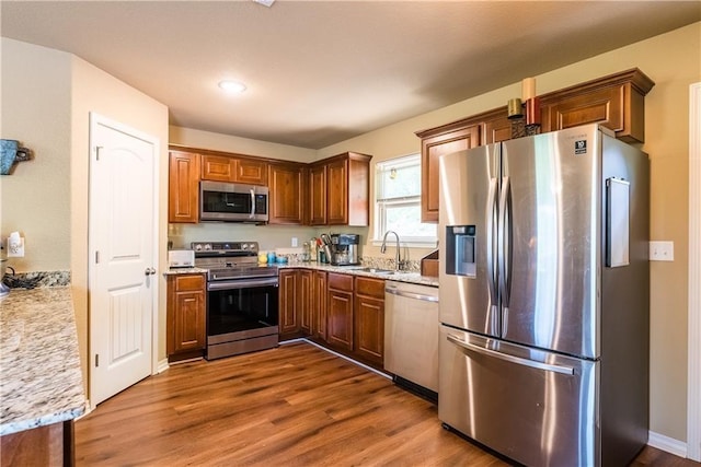 kitchen with appliances with stainless steel finishes, dark wood-style flooring, a sink, and light stone counters