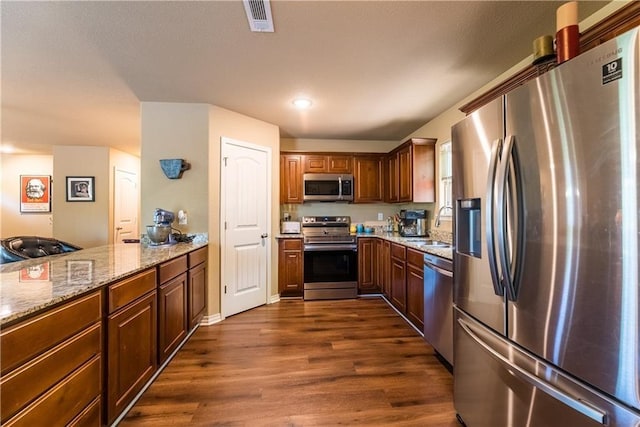 kitchen featuring visible vents, dark wood-type flooring, light stone countertops, stainless steel appliances, and a sink