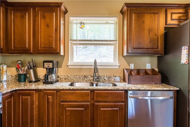 kitchen featuring appliances with stainless steel finishes, a sink, and light stone countertops