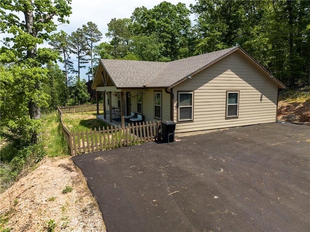 view of front of home with covered porch, roof with shingles, fence, and driveway