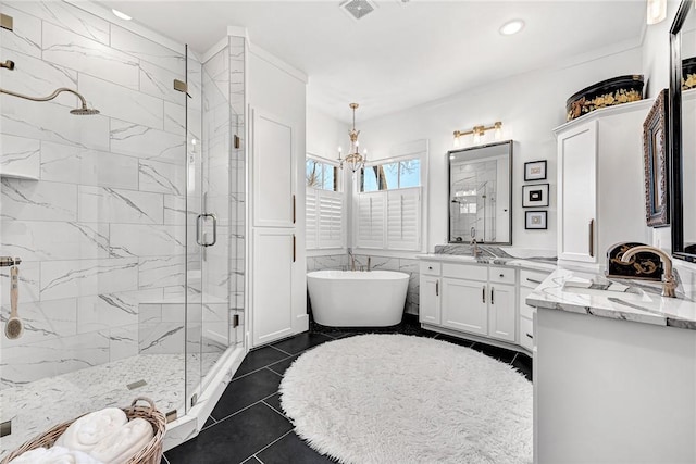 full bath with a freestanding tub, visible vents, two vanities, a marble finish shower, and tile patterned flooring