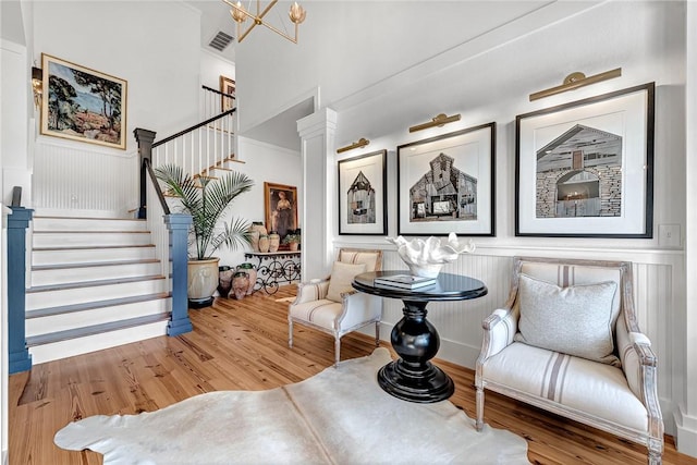 sitting room featuring stairway, wood finished floors, visible vents, decorative columns, and a decorative wall